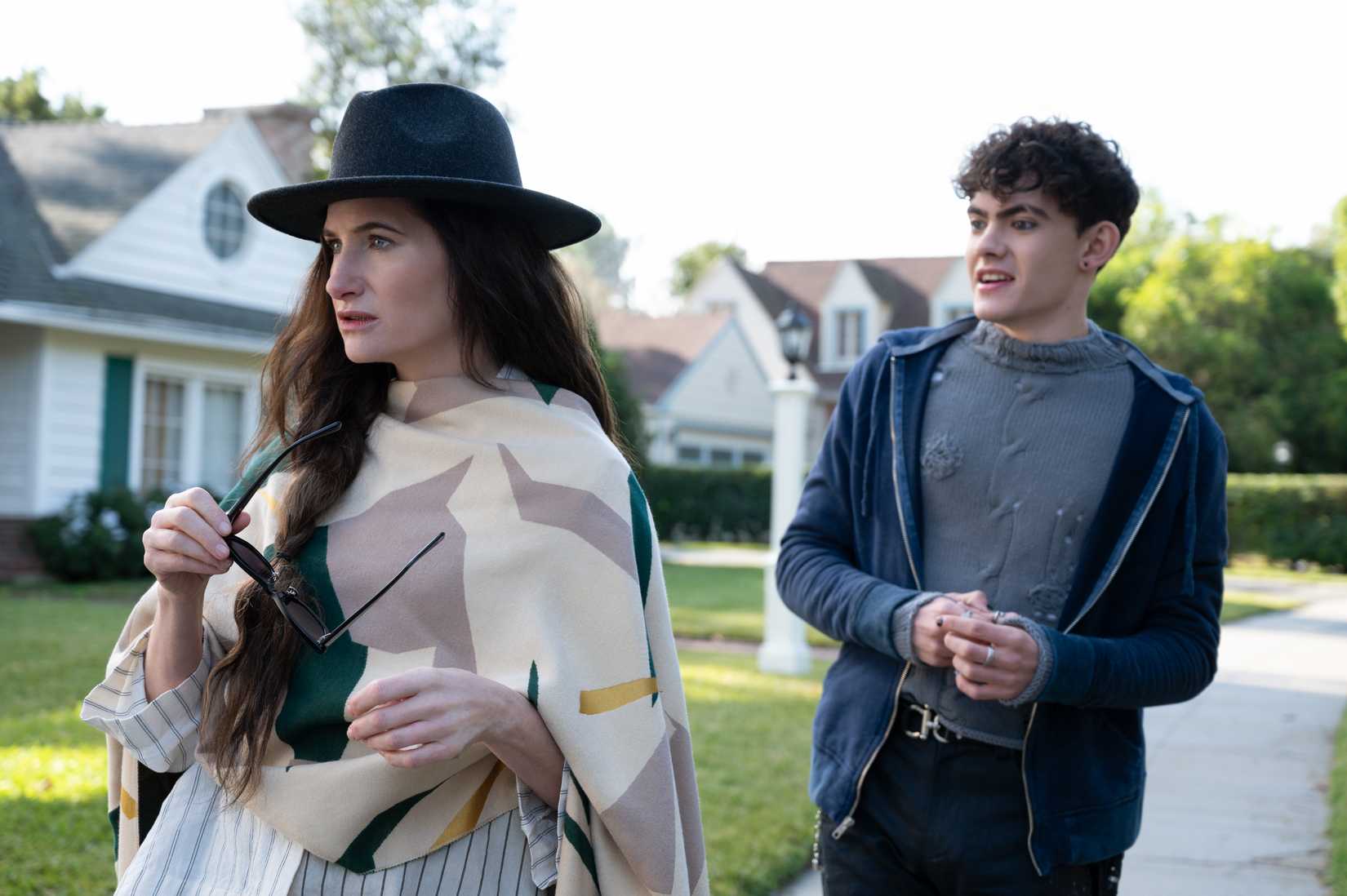 (R-L): Teen (Joe Locke) and Agatha Harkness (Kathryn Hahn) in Agatha All Along. They’re walking down a suburban street together, and Teen looks confused.