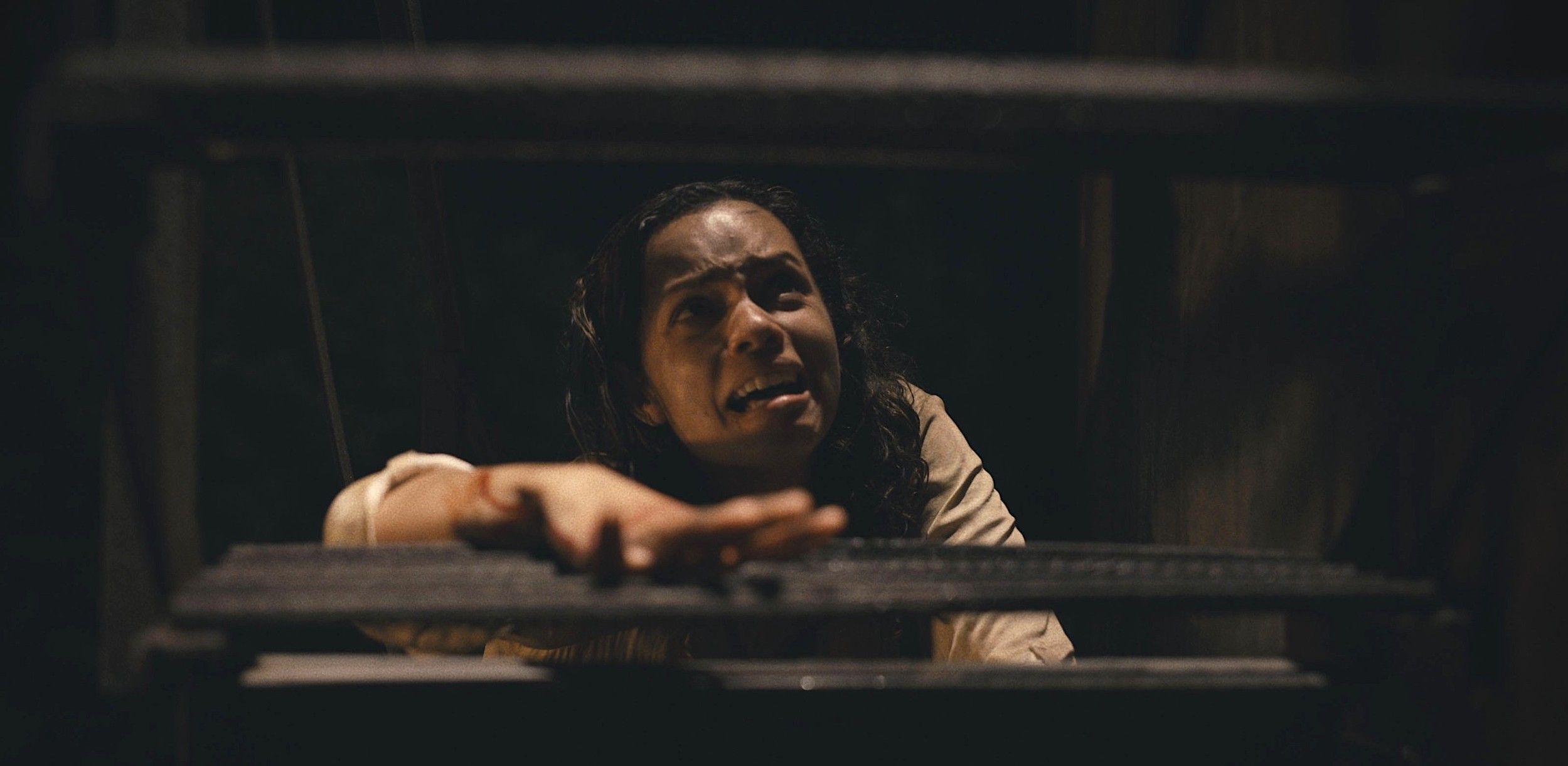 Tess (Georgina Campbell) crawls up a set of dark wooden stars, crying, in Barbarian