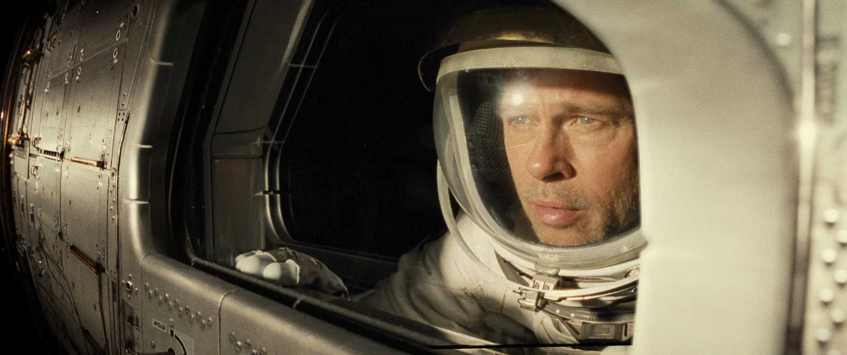Brad Pitt in an astronaut suit looking out of the side of a porthole window in Ad Astra.