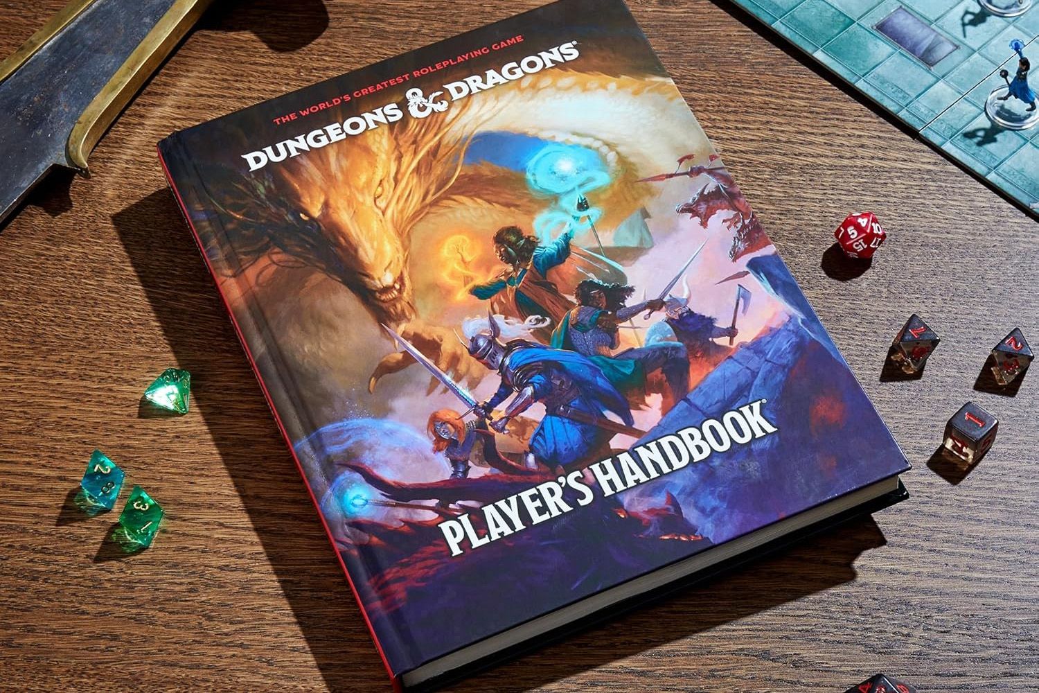 A copy of the 2024 Dungeons & Dragons Players Handbook on a table surrounded by various dice. There’s a playmat to the top right and a replica sword barely seen to the top left
