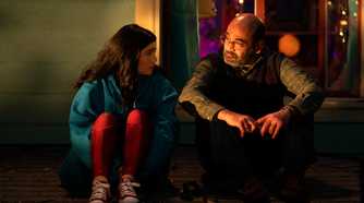 Kamala and her father sitting together on the floor. Kamala has her knees pulled to her chest and looks a bit nervous, while her father looks understanding. From Ms. Marvel.