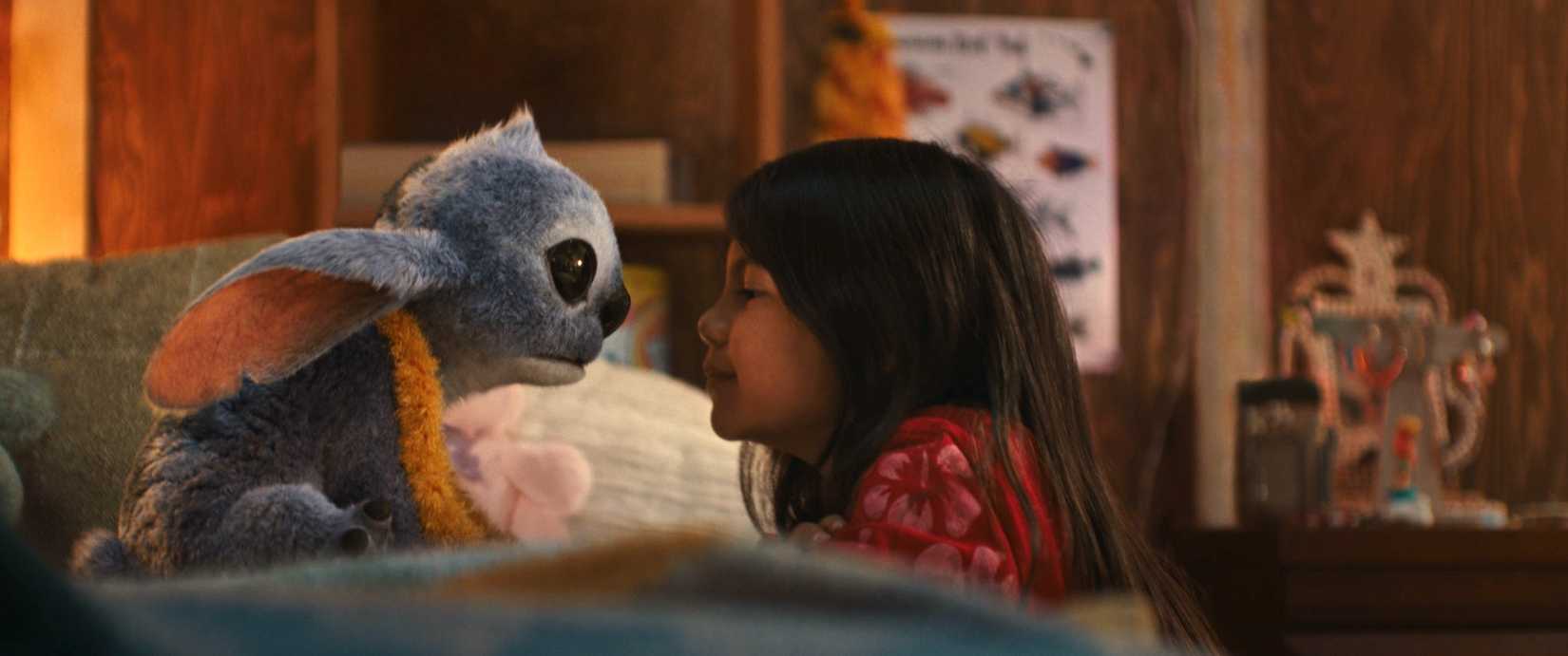 Stitch and Maia Kealoha as Lilo in Disney’s live-action Lilo & Stitch. They’re cutely bumping noses on a bed.