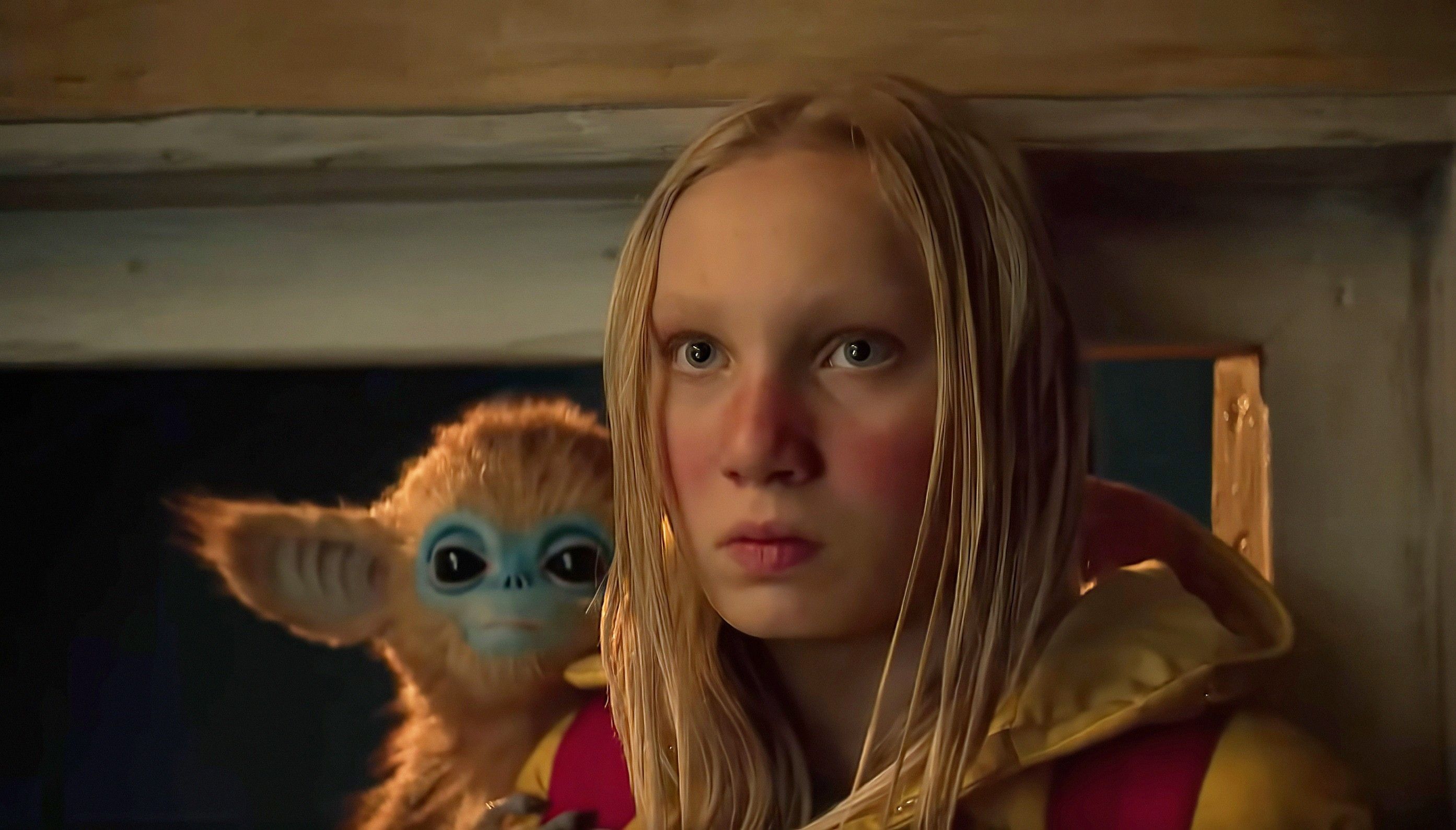 A blonde girl looks determined, a tiny golden monkey creature perched on her shoulder. From The Legend of Ochi