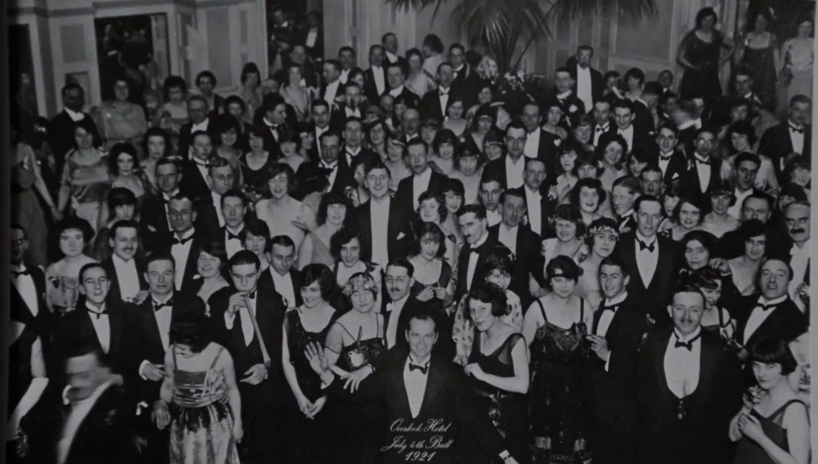 A black and white photo from the end of The Shining with Jack Nicholson at the front of a party full of people in a ballroom