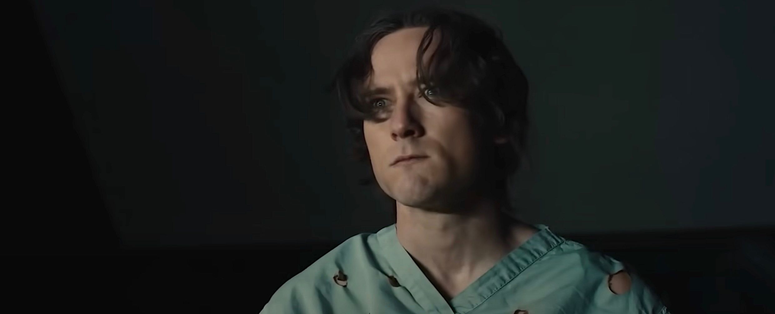 Lewis Pullman as Bob in the Thunderbolts trailer, wearing shot-up hospital scrubs, his eyes just starting to glow with a dim gold light