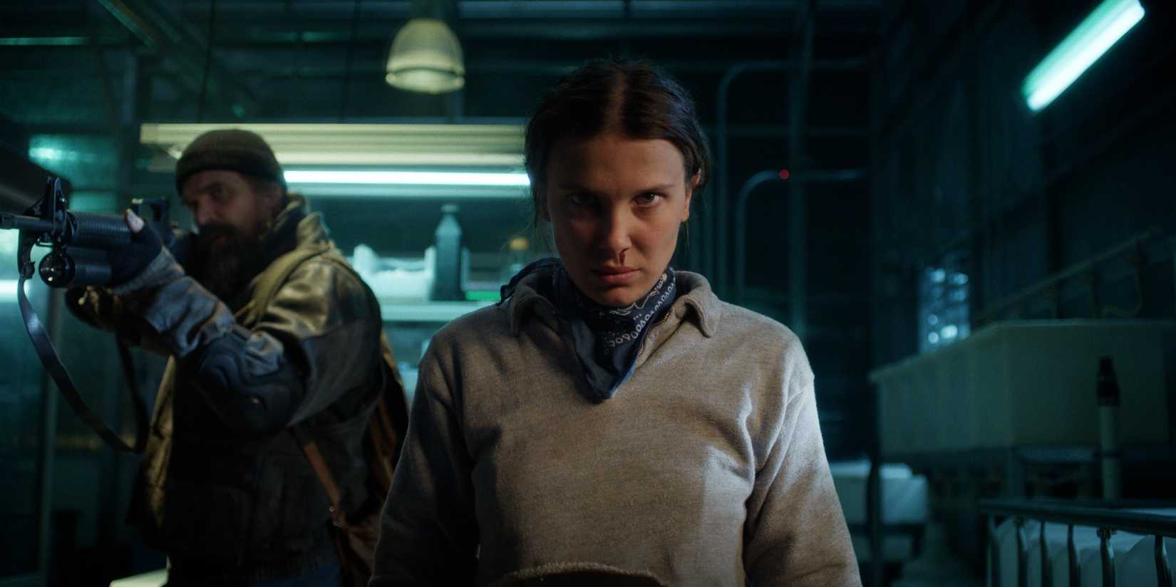 David Harbour as Jim Hopper holding a shotgun stands behind and Millie Bobby Brown as Eleven with a nosebleed in season 5 of Stranger Things