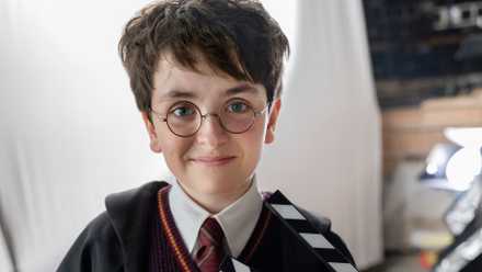 Dominic McLaughlin dressed as Harry Potter in his Hogwarts robes, holding a clapboard
