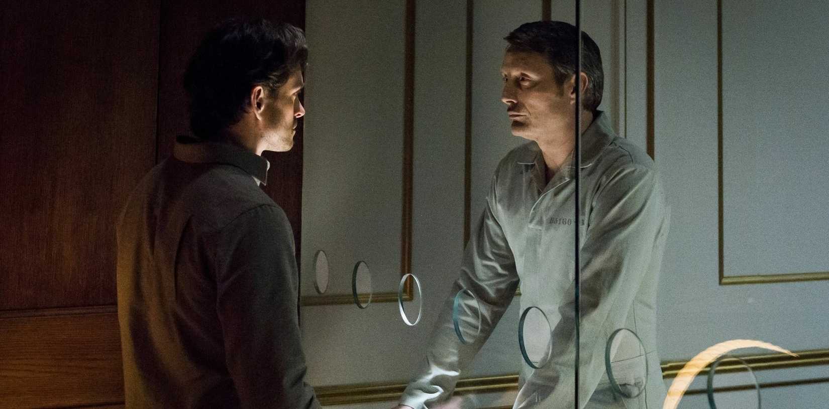 Hannibal Lecter (Mads Mikkelsen) faces Will Graham (Hugh Dancy) with a prison glass screen full of round speaking holes