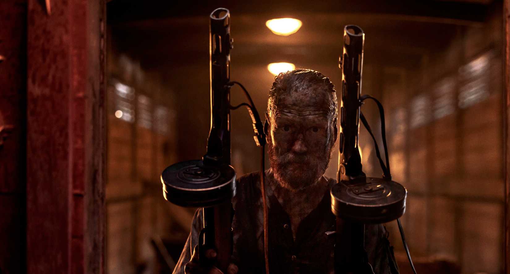 Finnish army veteran Aatami Korpi (Jorma Tommila), covered in blood and filth, stands in a dark train car holding two enormous guns in Sisu: Road to Revenge