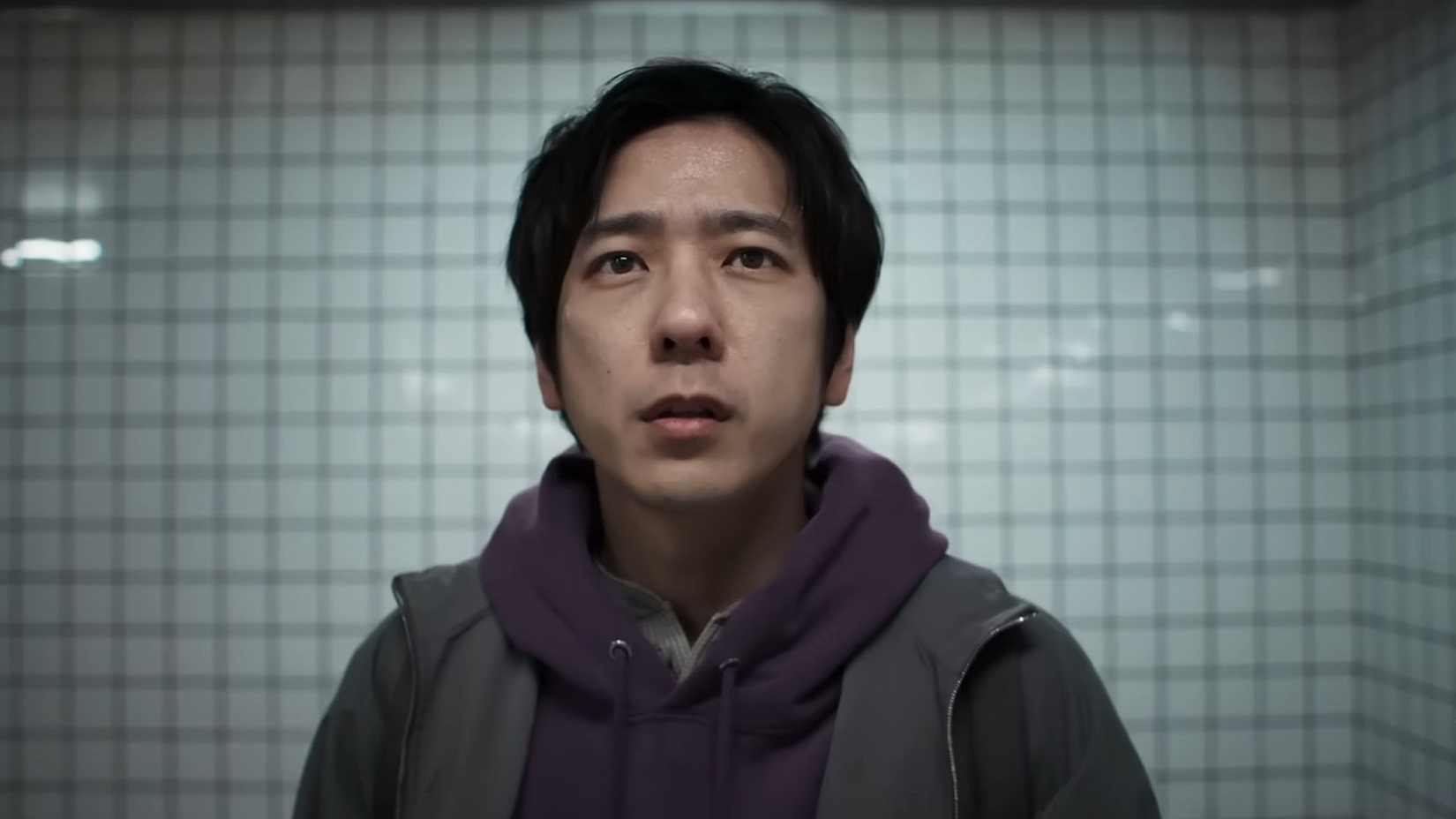 A screenshot from the Exit 8 trailer showing the protagonist, a Japanese man wearing a hoodie