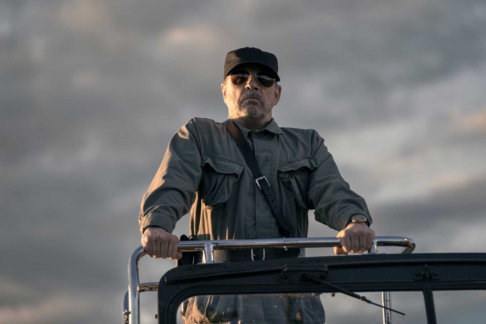 El mayor (Mark Hamill), un hombre con un uniforme militar gris, un sombrero negro y gafas de sol opacas, se encuentra en la parte trasera de un vehículo en la larga caminata