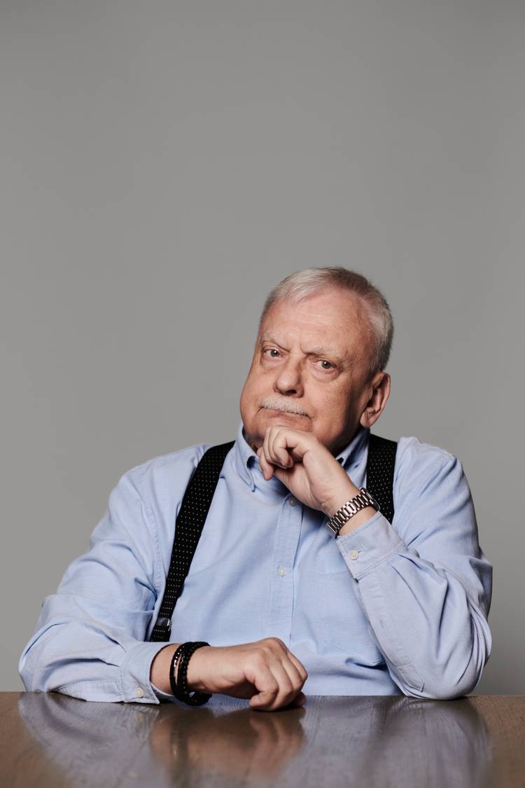 चुड़ैल लेखक Andrzej Sapkowski एक ग्रे बैकड्रॉप के सामने अपने हाथ पर अपनी ठुड्डी के साथ बैठता है