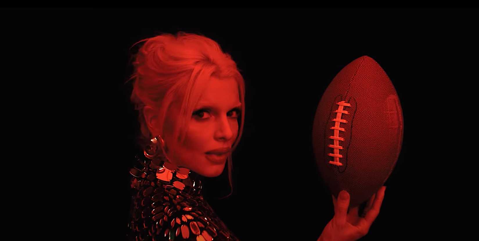 Julia Fox in Him, holding a football, lit in red light