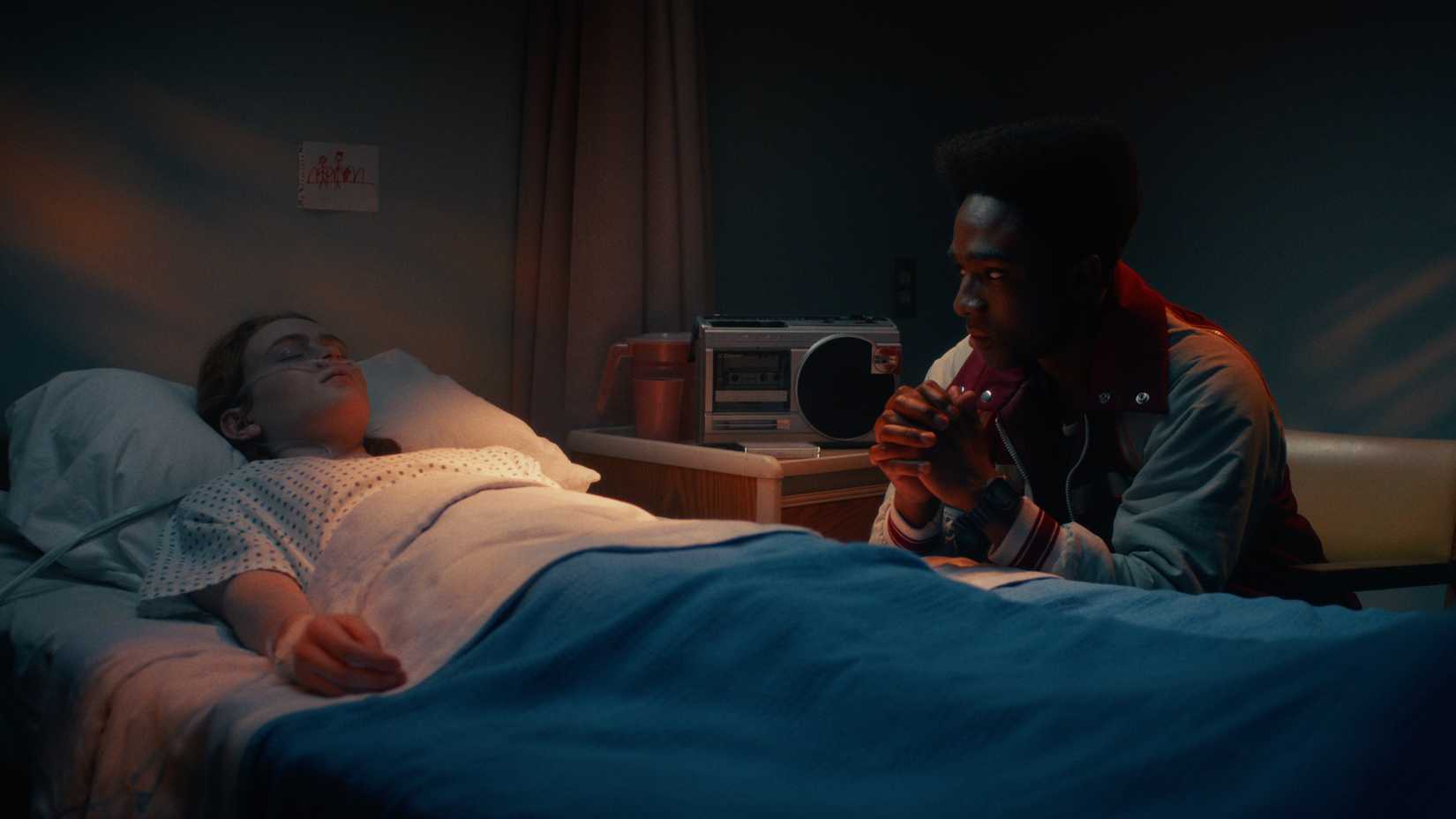 मैक्स मेफील्ड (सैडी सिंक) एक अस्पताल के बिस्तर में लुकास सिनक्लेयर (कालेब मैकलॉघलिन) के साथ उसकी तरफ बैठे हैं