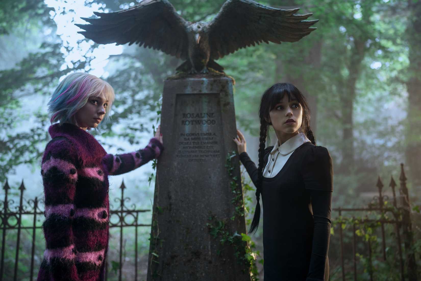 Image from Wednesday season 2. Both Enid and Wednesday place their hand on what a headstone.