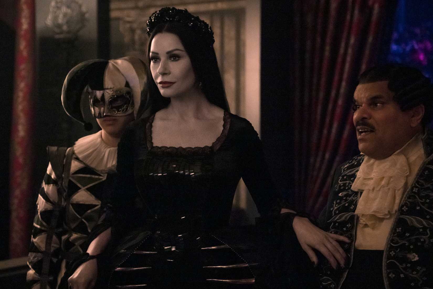 Image from Netflix's Wednesday. Morticia stands in front of Gomez and Pugsley, a protective hand over Gomez's cravat.