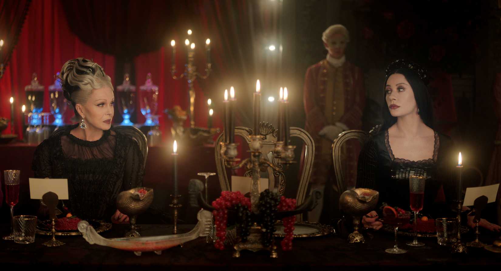 Wednesday image featuring Hester and her daughter, Morticia. They stare at one another across a dining table.