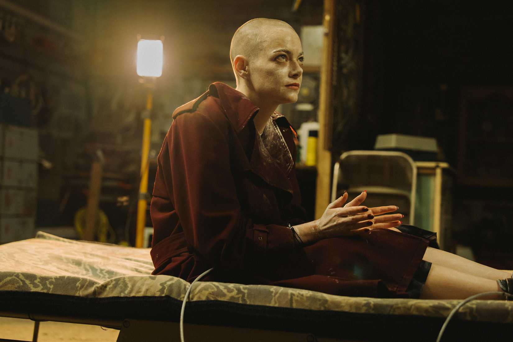 Emma Stone, bald and pale, tied down to a bed in a dimly lit basement in Bugonia