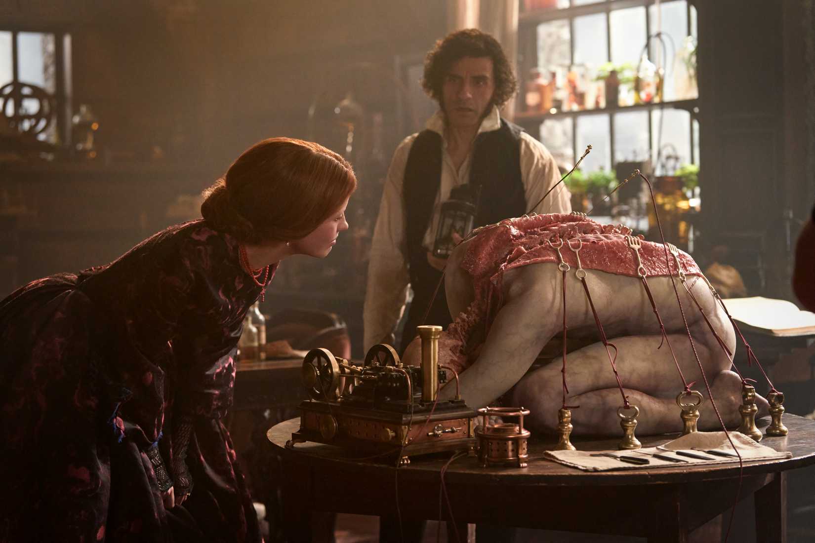 Elizabeth (Mia Goth) examines a corpse on a table while Frankenstein (Oscar Isaac) looks on