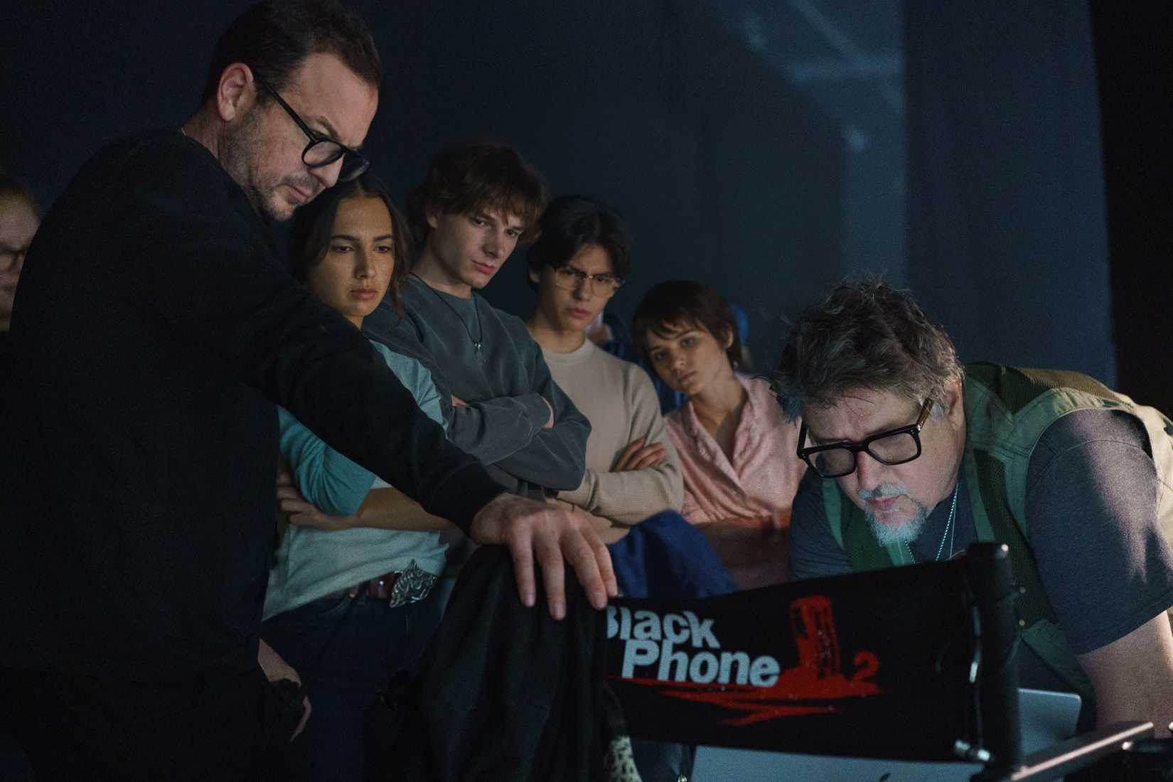Executive Producer Jason Blumenfeld, actors Arianna Rivas, Mason Thames, Miguel Mora, and Madeleine McGraw, and director Scott Derrickson gather around a laptop on the set of Black Phone 2