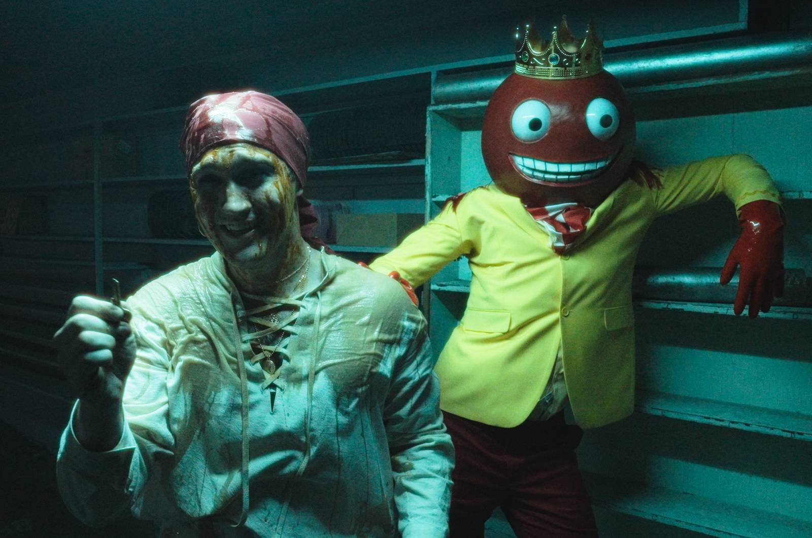 A man in pirate costume, smeared with grime, holds up a key as a gumball-headed creature in a yellow jacket leans against a wall behind him