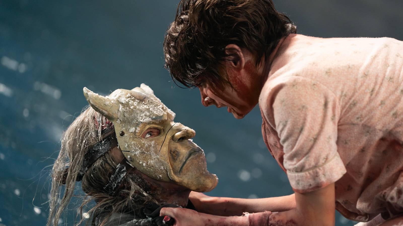 A bloodied, battered Gwen (Madeleine McGraw) grabs the masked serial killer The Grabber (Ethan Hawke) by the collar in Black Phone 2