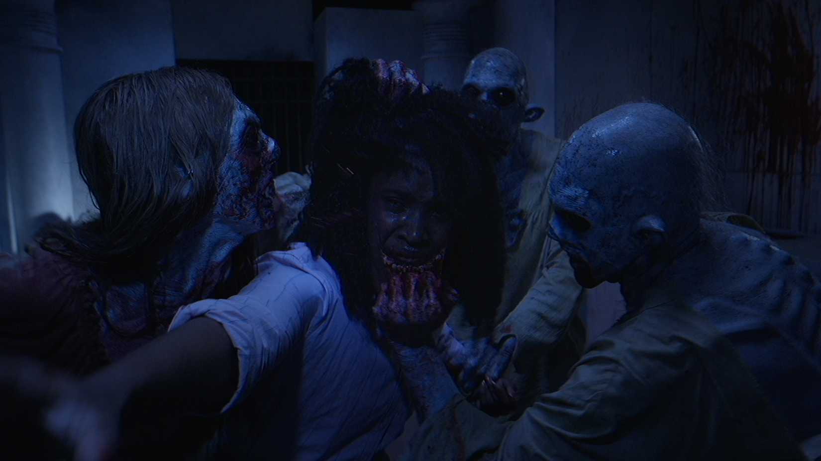 Two ghoulish, blood-spattered figures rip at the face of a crying teenager in a dark hallway as a third lurks behind in the V/H/S Halloween short "Home Haunt"