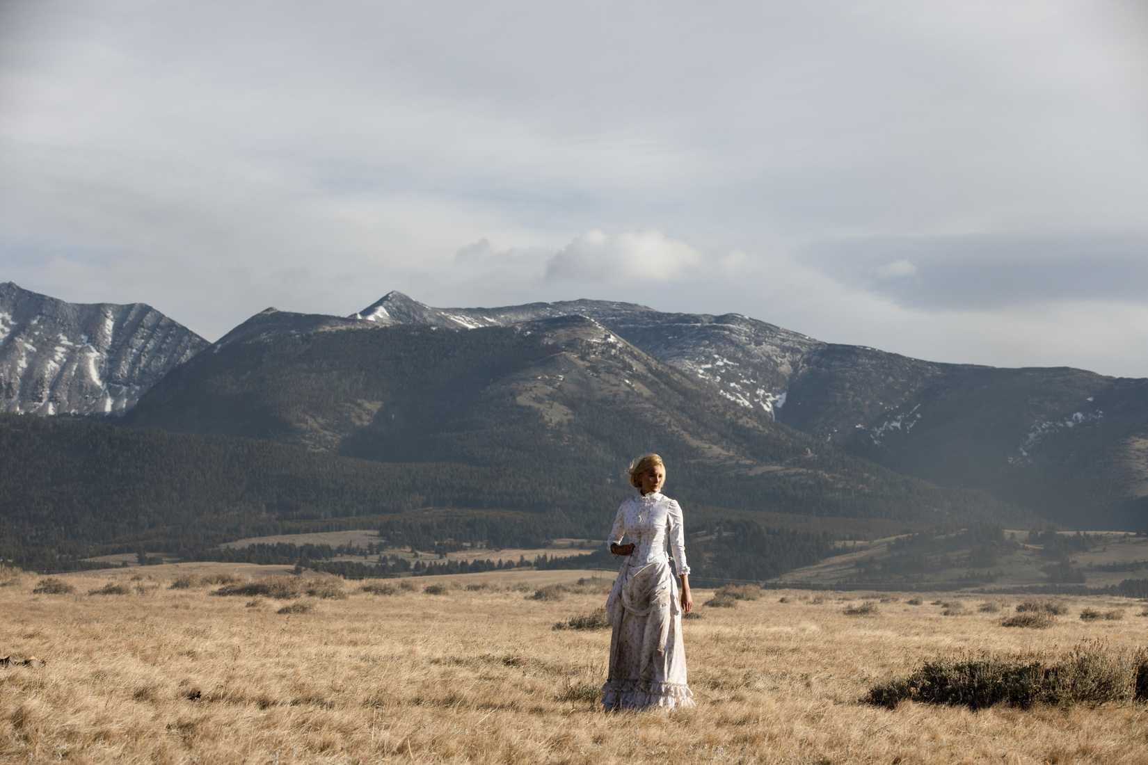 Elsa (Isabel May) fica em um campo vazio com montanhas em segundo plano em 1883