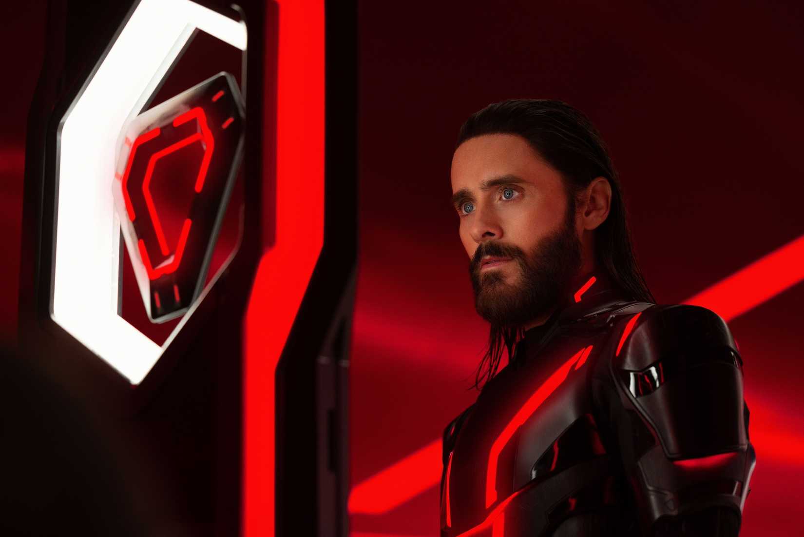 Ares (Jared Leto, em um terno preto) fica em um espaço de néon com iluminação vermelha em Tron: Ares
