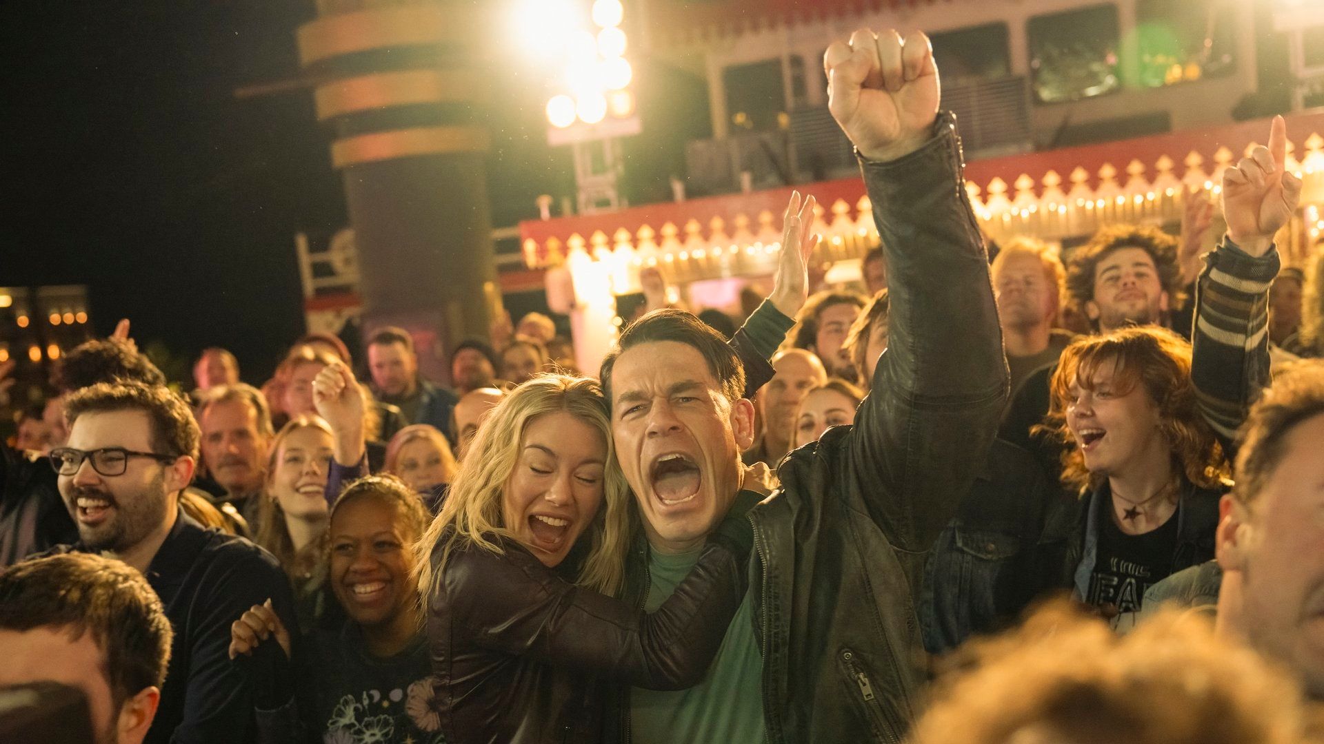 Emilia Harcourt (Jennifer Holland) hugs Chris Smith (John Cena) who cheers during a concert on a boat in Peacemaker