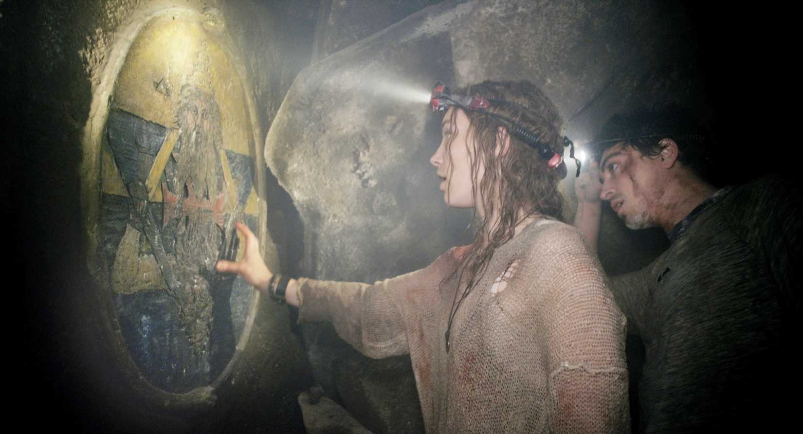 Two disheveled, blood-smeared people (Perdita Weeks and Ben Feldman) shine flashlights on an old-looking occult symbol on a wall in As Above, So Below