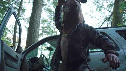 Johnny, a hulking man in a filthy leather jacket and diving-bell helmet, raises his axe to attack in In a Violent Nature