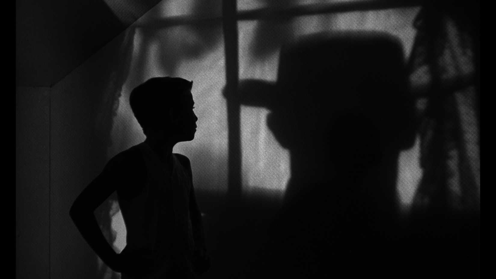 A shadowy man in a hat stalks a silhouetted boy in Night of the Hunter