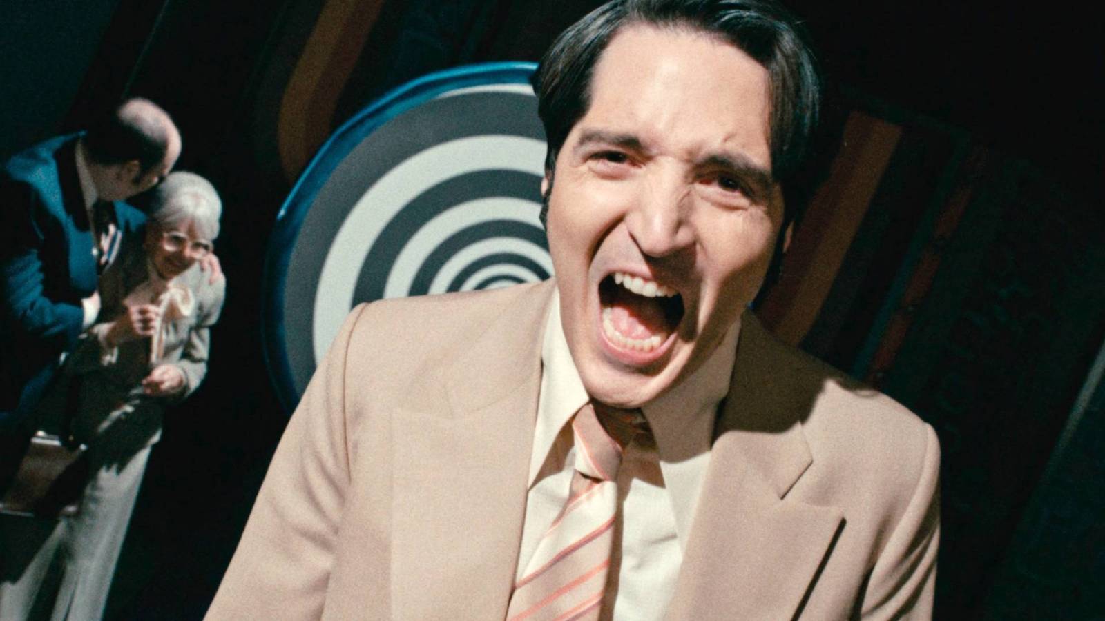 Talk-show host Jack Delroy (David Dastmalchian) shouts into the camera in Late Night With The Devil, framed by a spiraling TV backdrop