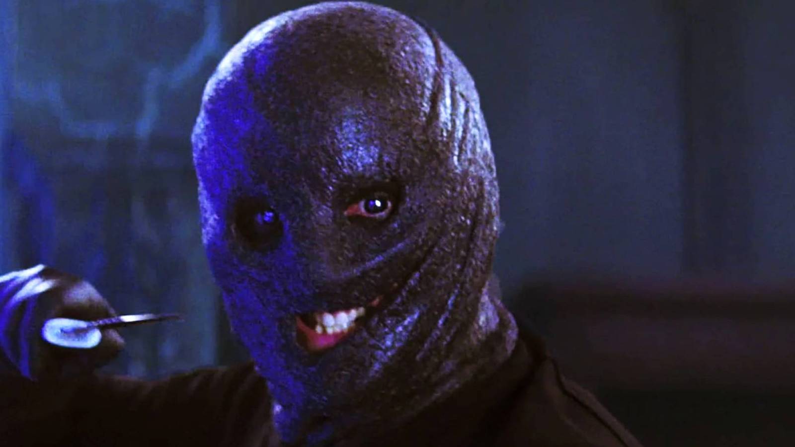 A grinning person in a shapeless, fat hood holds a sharp object in the 2009 film, a collector