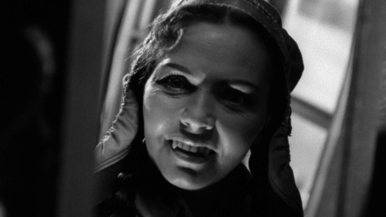 The black and white image of a woman dressed in a traditional Finnish hat and a vampire’s sports teeth in a white deer
