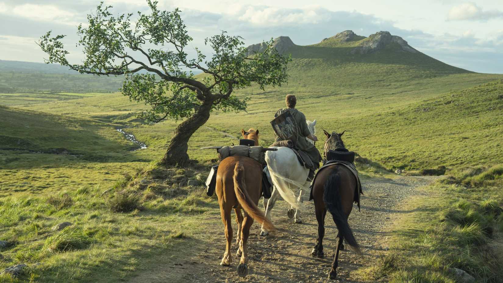 Peter Claffey as Dunk riding horseback with two horses behind on a grassy rode in A Knight of the Seven Knigdoms