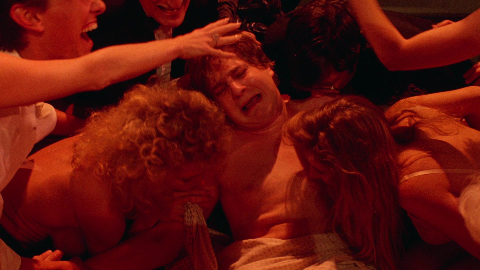 A man looks distressed as people writhe all around him under red lighting in Society