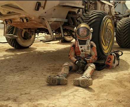 Matt Damon at Mark Watney leans against a Mars rover in the Martian