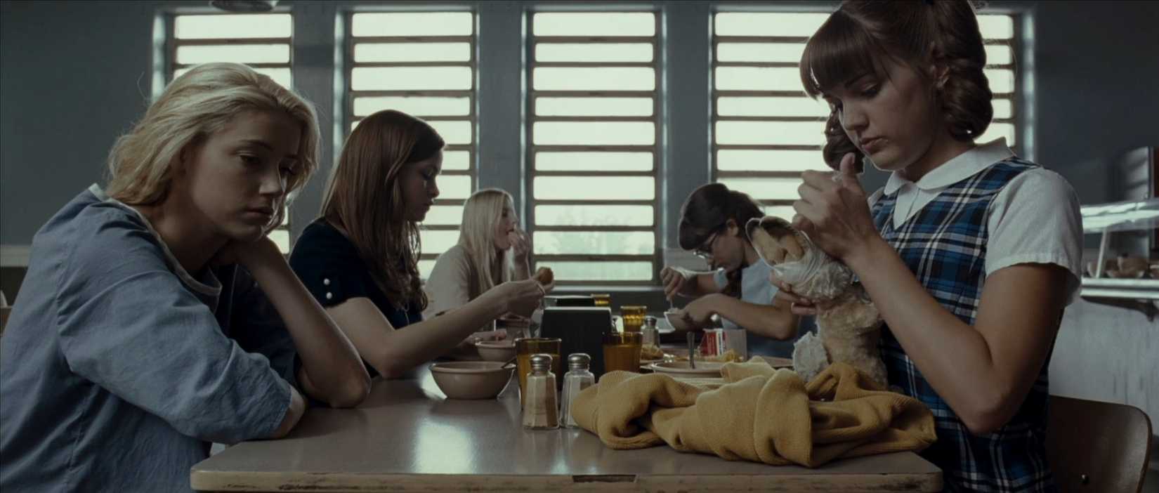 A widescreen shot of the female patients of the psychiatric ward seated at a long table in John Carpenter's The Ward.