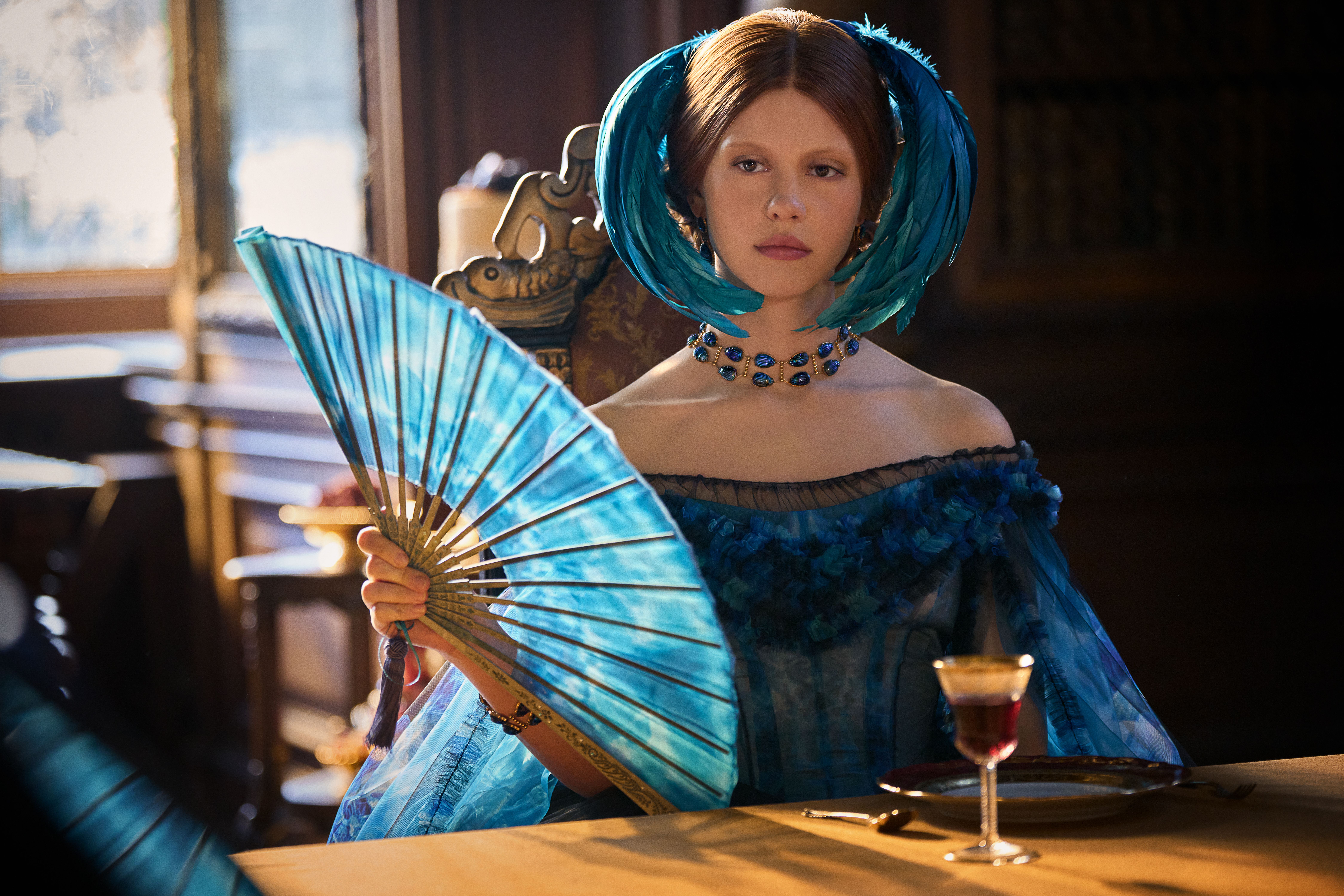Mia Goth wearing a blue dress and holding a matching fan in Frankenstein
