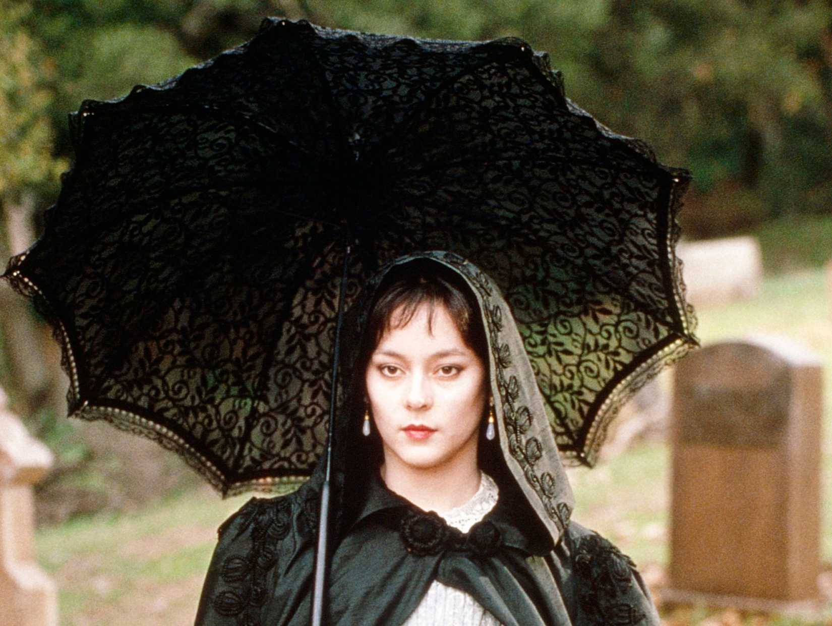 Meg Tilly as Carmilla, a dark-haired, predatory-looking woman under a black umbrella, in the 1989 film Nightmare Classic.