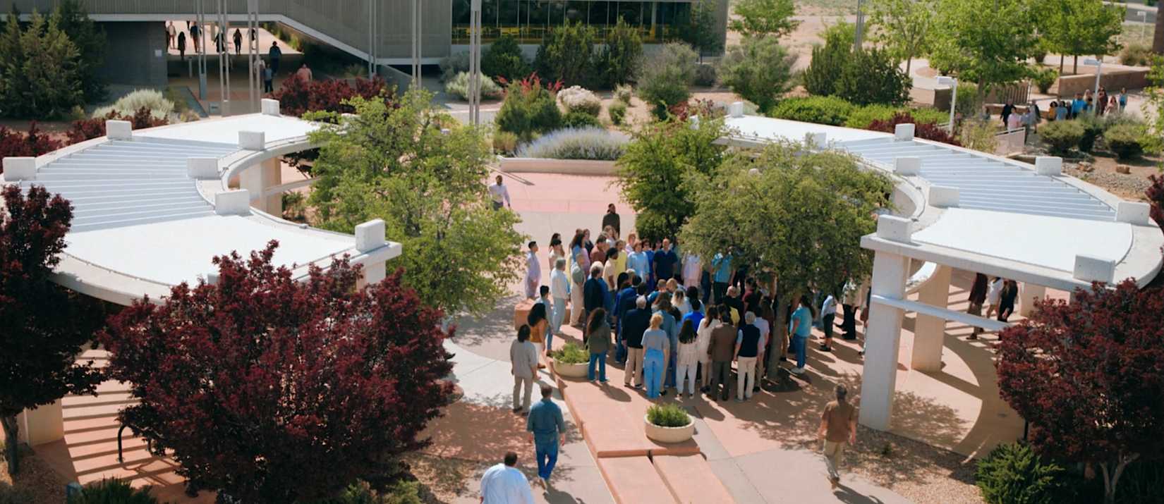 A group of Others coalesce around Carol (Rhea Seehorn) in a public park in Pluribus episode 4