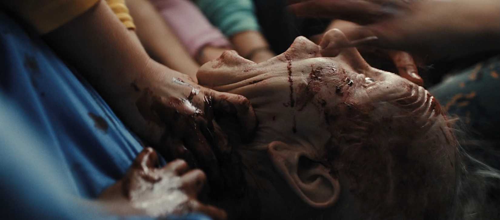 A close-up of a woman's bloody, screaming face as a mob of children pull at her from all sides in Weapons