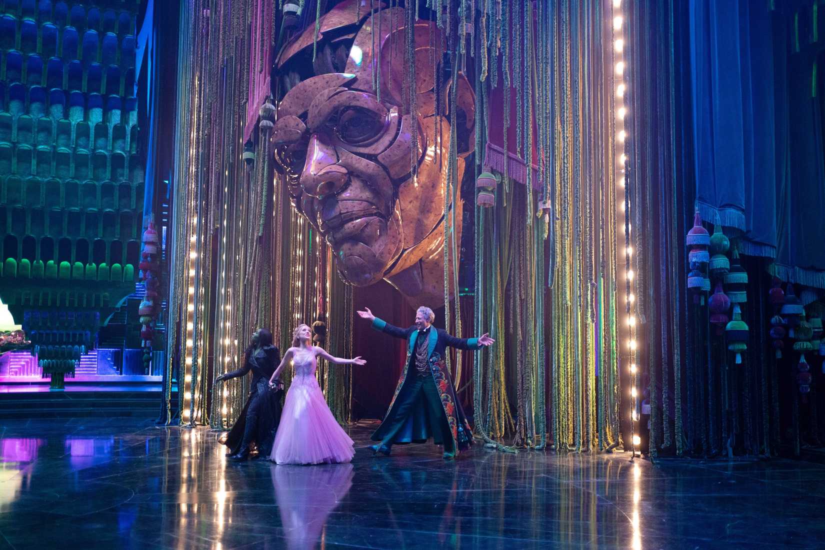 Elphaba (Cynthia Erivo), Glinda (Ariana Grande) and the Wizard of Oz (Jeff Goldblum) all dance together in his audience chamber, dwarfed by the huge artificial Wizard of Oz head, in Wicked: For Good