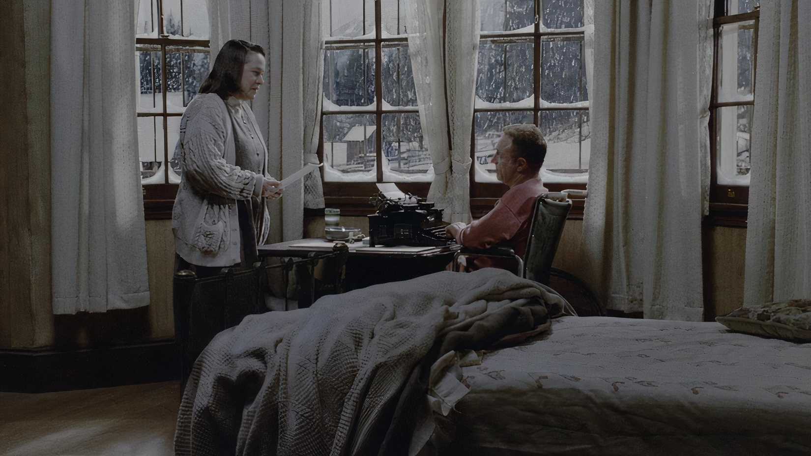 And injured Paul sits at his typewriter as Annie reads through his latest draft.