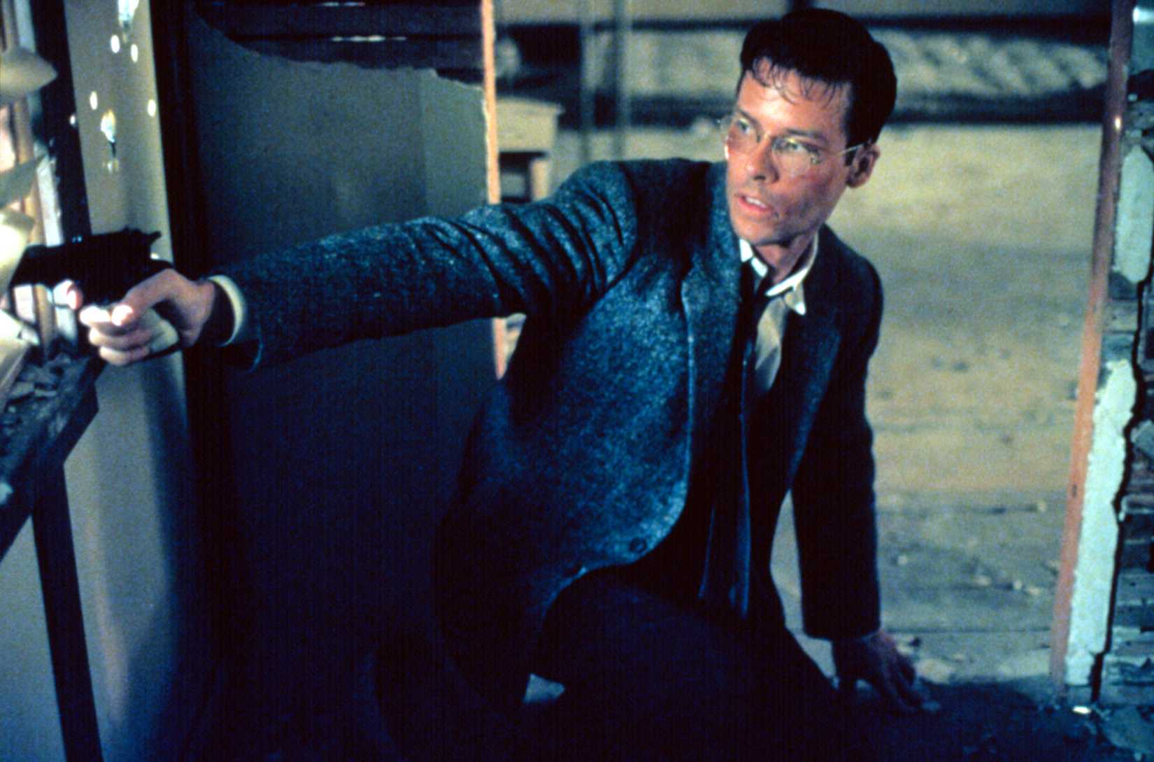 Guy Pearce, sweaty and bloodied, points a pistol off-screen in L.A. Confidential