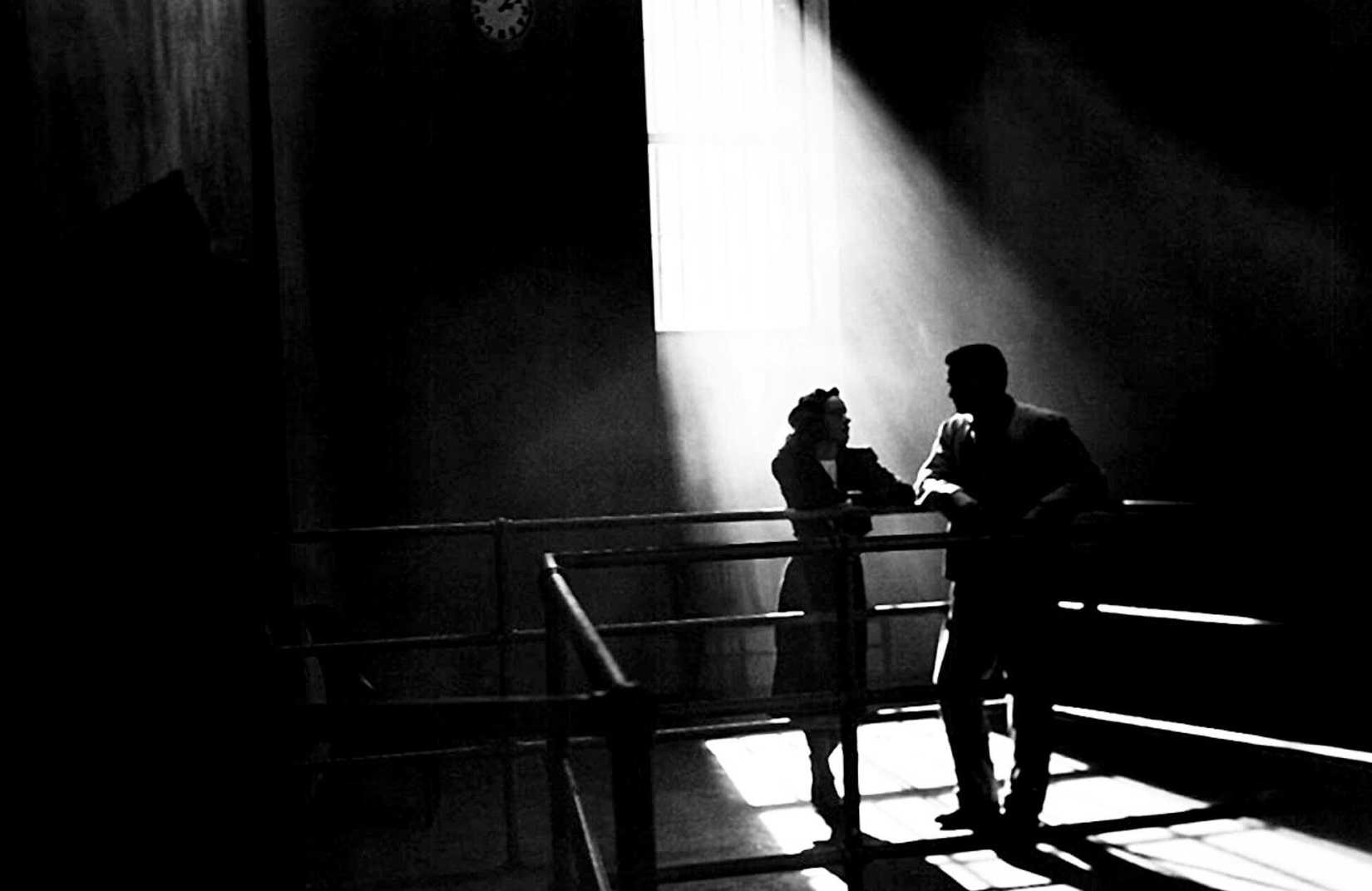 A man and a woman stand nearly silhouetted in a sunbeam in a dark black and white space in Phantom Lady