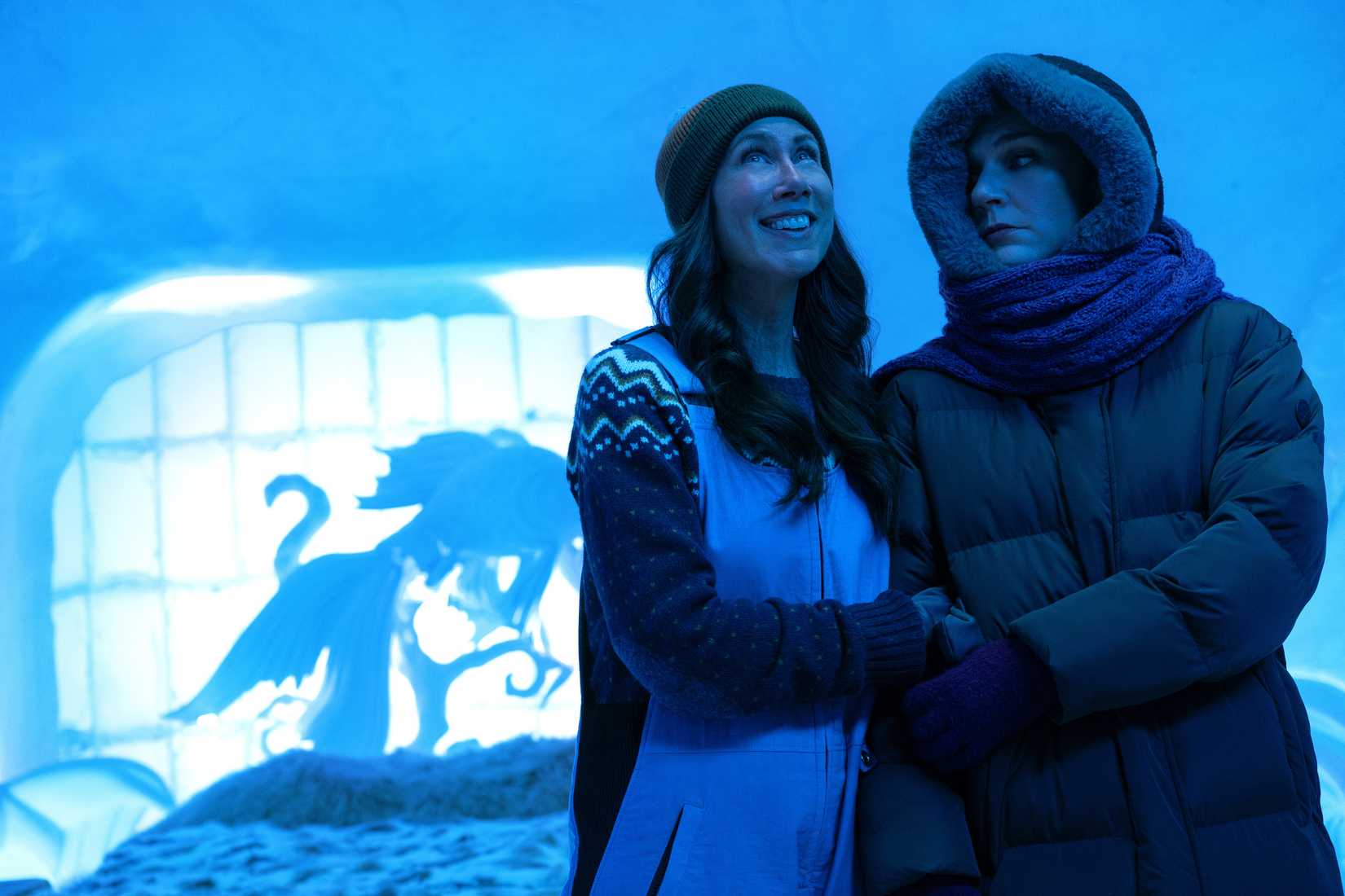 Helen and Carol (Miriam Shor and Rhea Seehorn), bundled up in coats in a blue-lit room in an ice hotel in Pluribus
