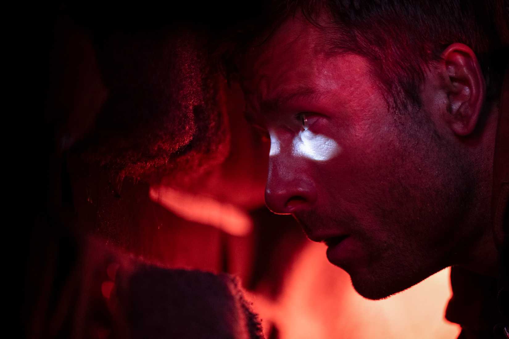 Ben Richards (Glen Powell), en el maletero de un automóvil con poca luz roja, mira a través de un agujero de bala hacia el exterior en la adaptación de 2025 de The Running Man de Stephen King.
